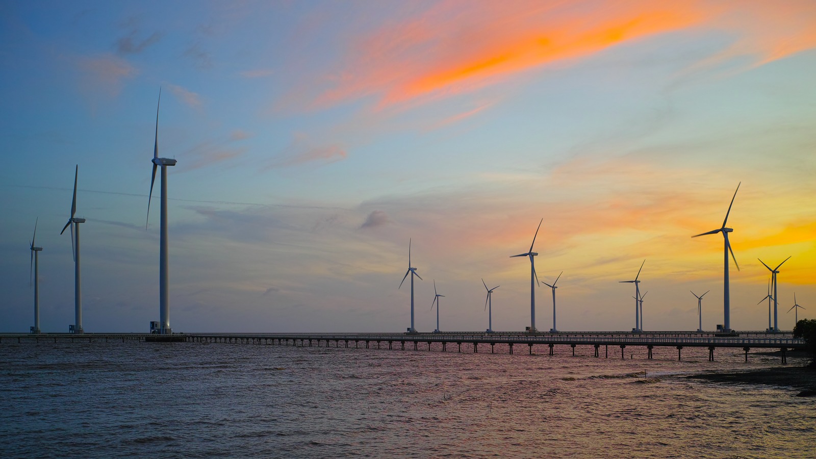 夕空の下、ベトナムの海沿いに並ぶ風力発電設備。海外の再エネ事業を表すイメージ写真。